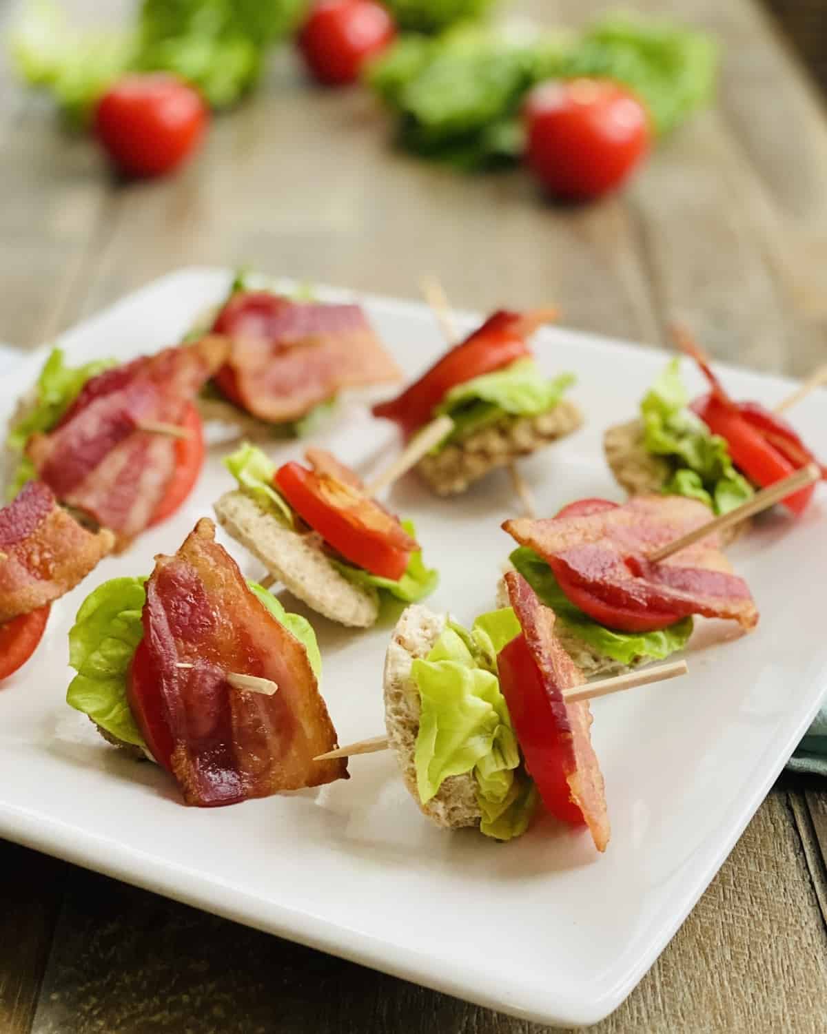 A white platter with bacon, lettuce and tomato appetizers.