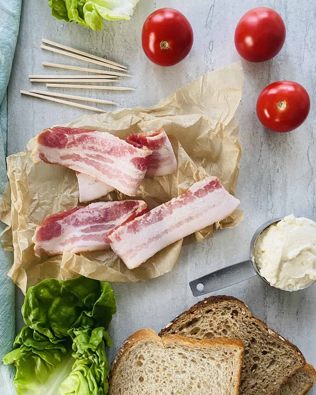 Bacon, tomatoes, lettuce, mayonnaise and slices of bread on a marble board.