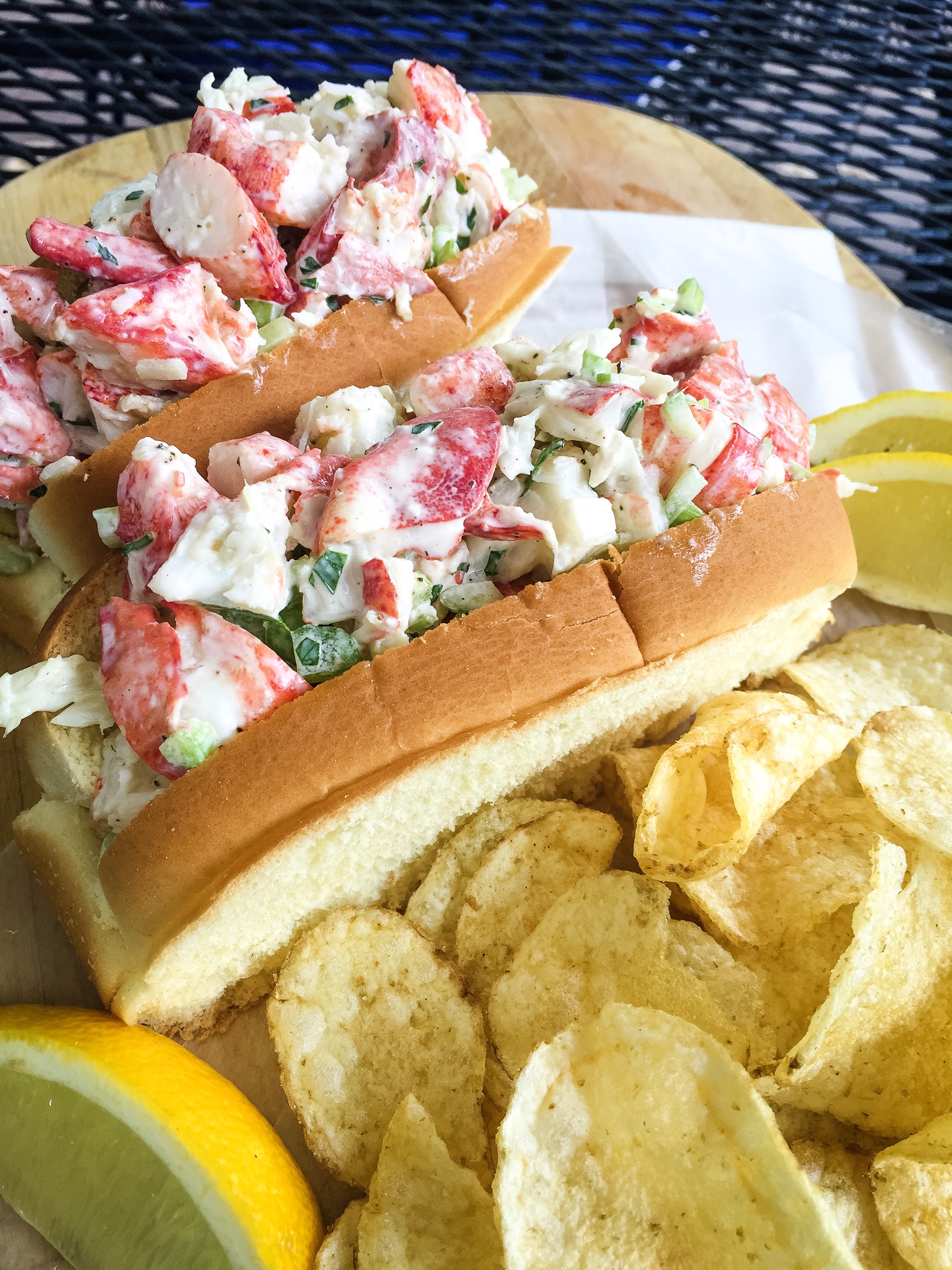 2 cold lobster rolls with potato chips and lemon wedges.