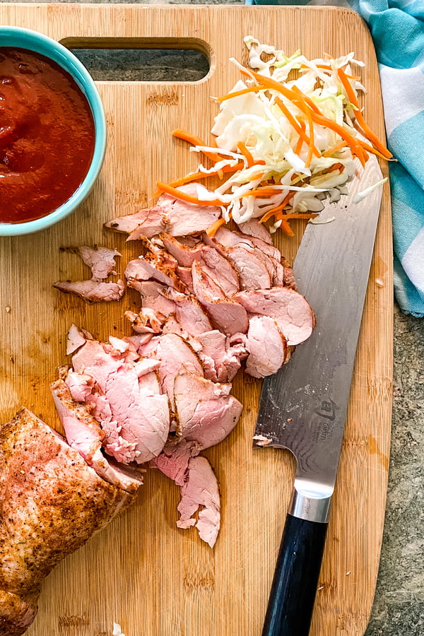 Sliced pork tenderloin and homemade barbecue sauce for sliders on a cutting board.