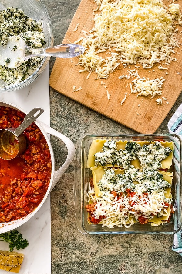 assembling a lasagna with layers of pasta, cheese, and Italian sausage tomato sauce