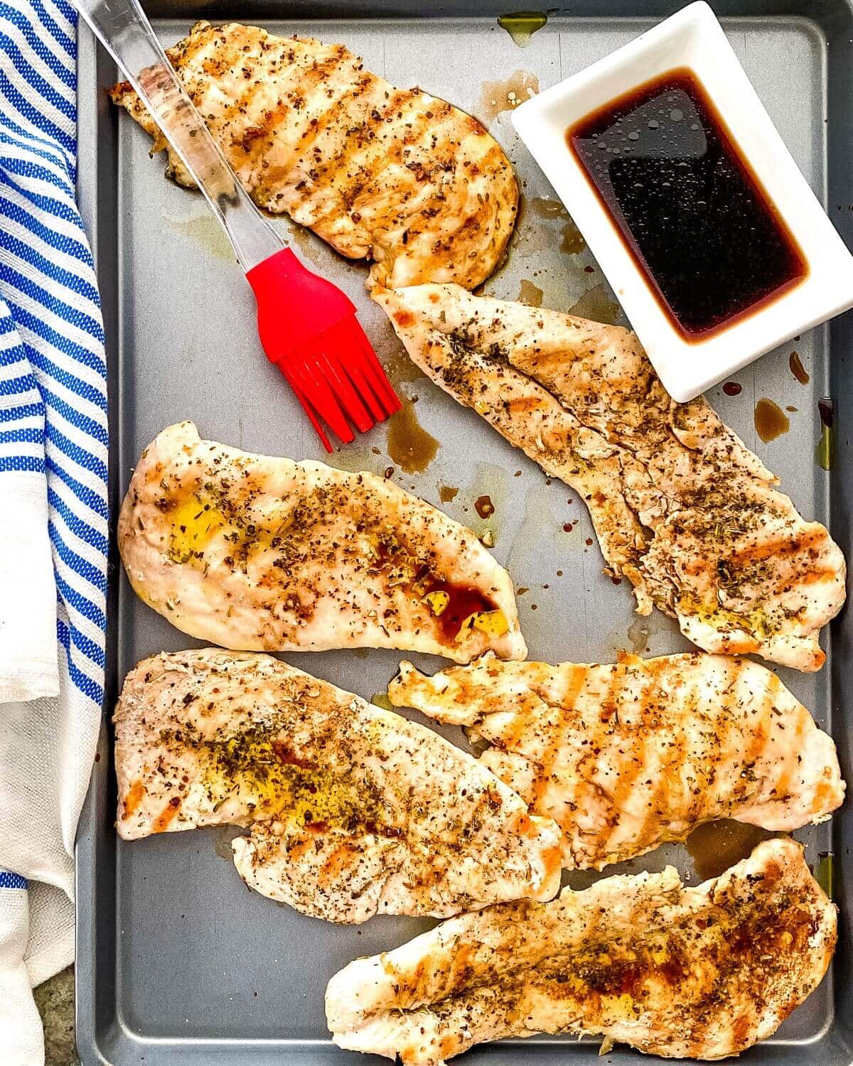 A sheet pan with balsamic vinegar, grilled chicken and a basting brush.