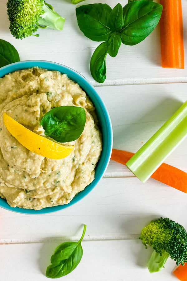 bowl of basil hummus with celery and carrot sticks