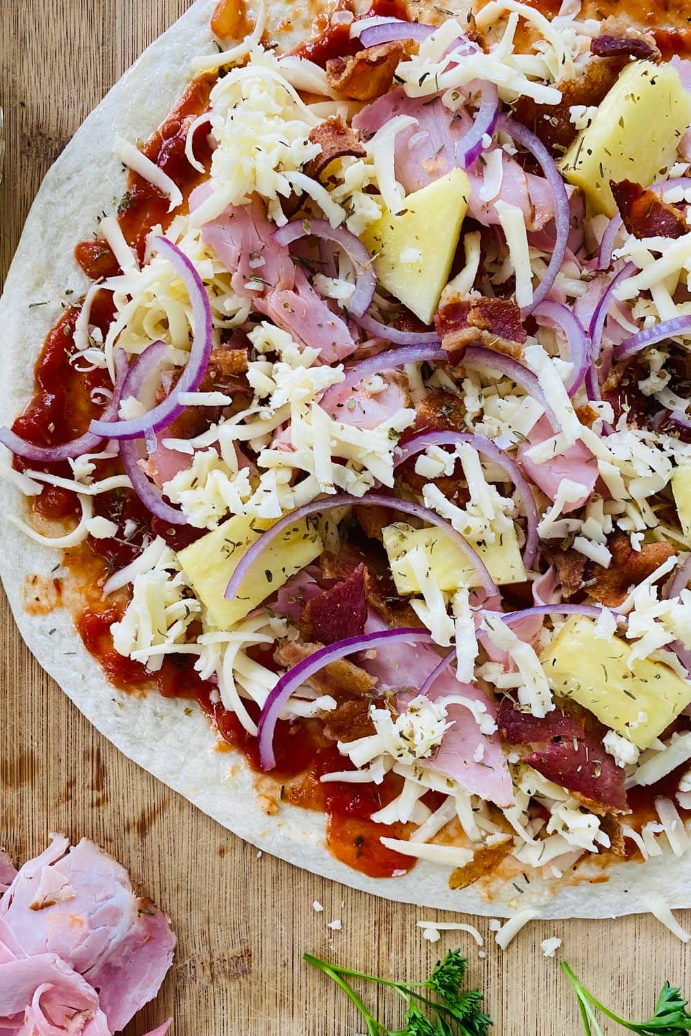 a tortilla pizza with ham, bacon and pineapple ready for the oven