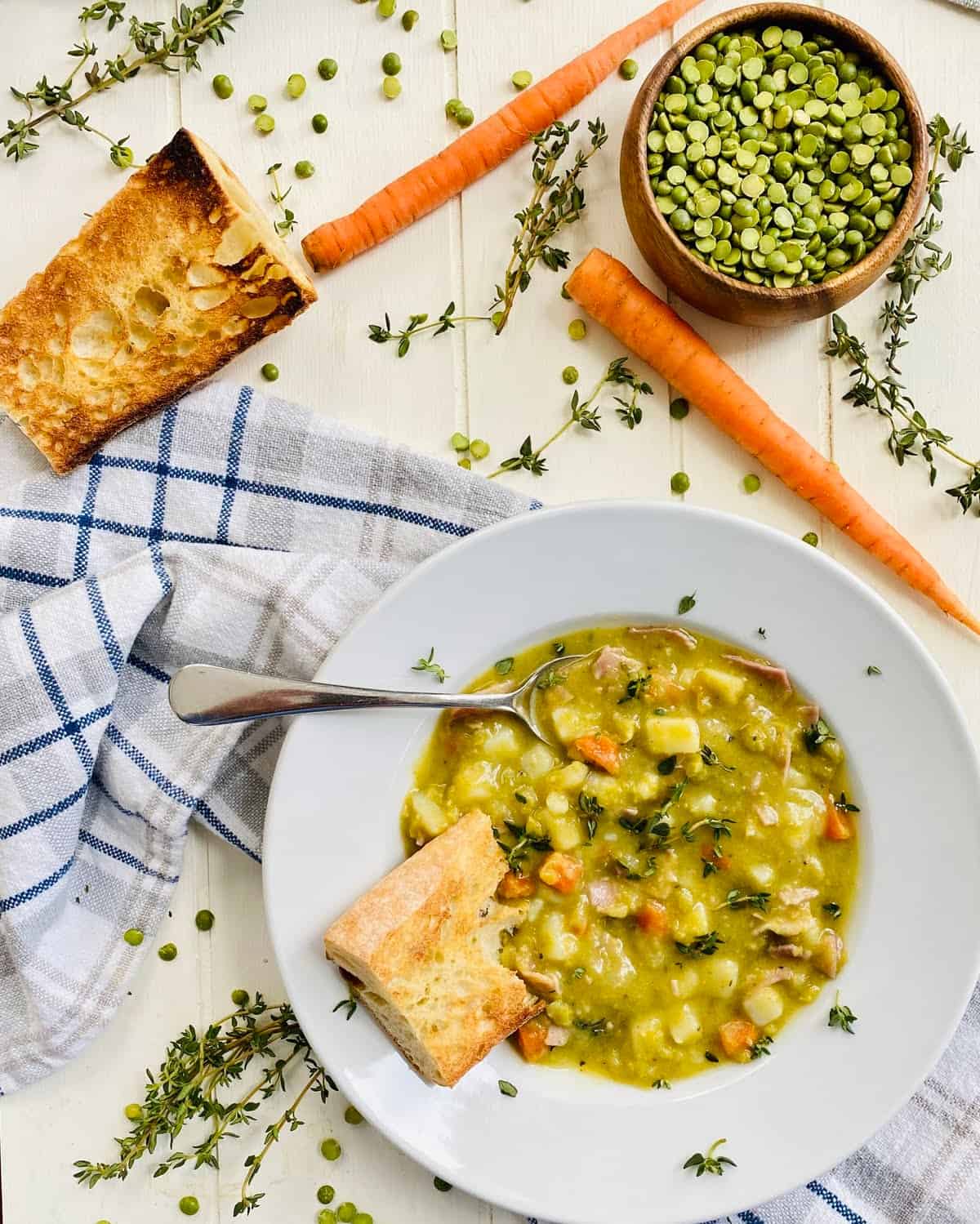 A bowl of split pea soup with ham and potatoes, 2 raw carrots and dried split peas.