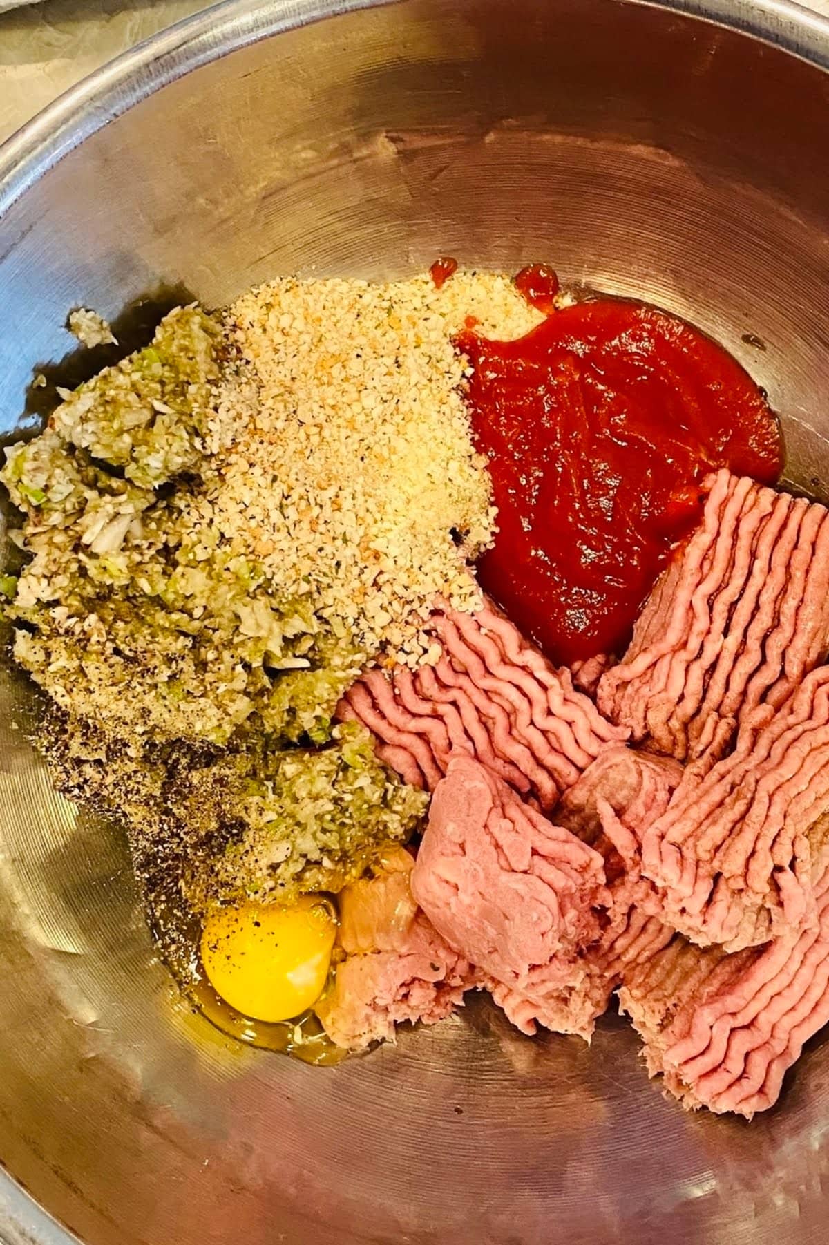 Ground turkey, ketchup, bread crumbs, egg, chopped vegetables and seasonings in a metal bowl.