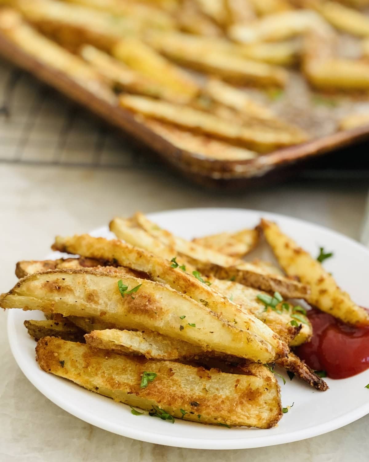 Plate with crispy oven fries and a baking sheet.