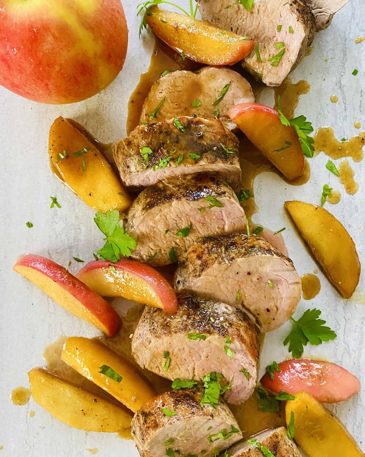 A sliced pork tenderloin drizzled with maple glaze and with sautéed apples.