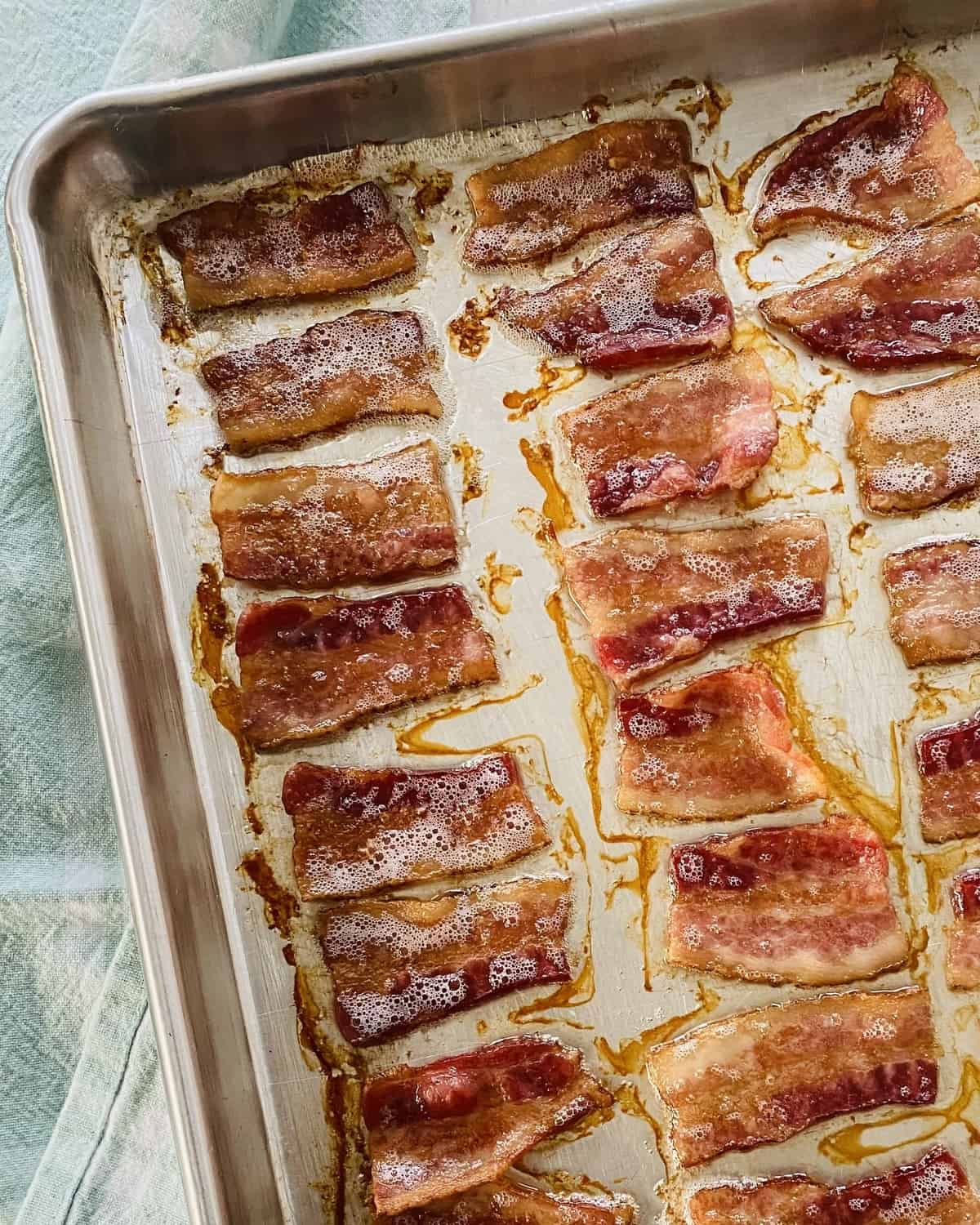 Cooked crispy pieces of bacon on a baking sheet.