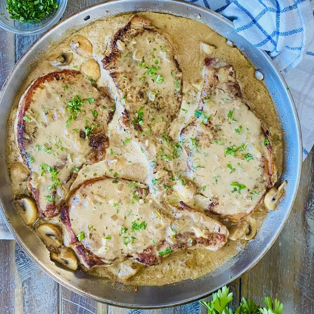 4 pork chops in a sauté pan with gravy.