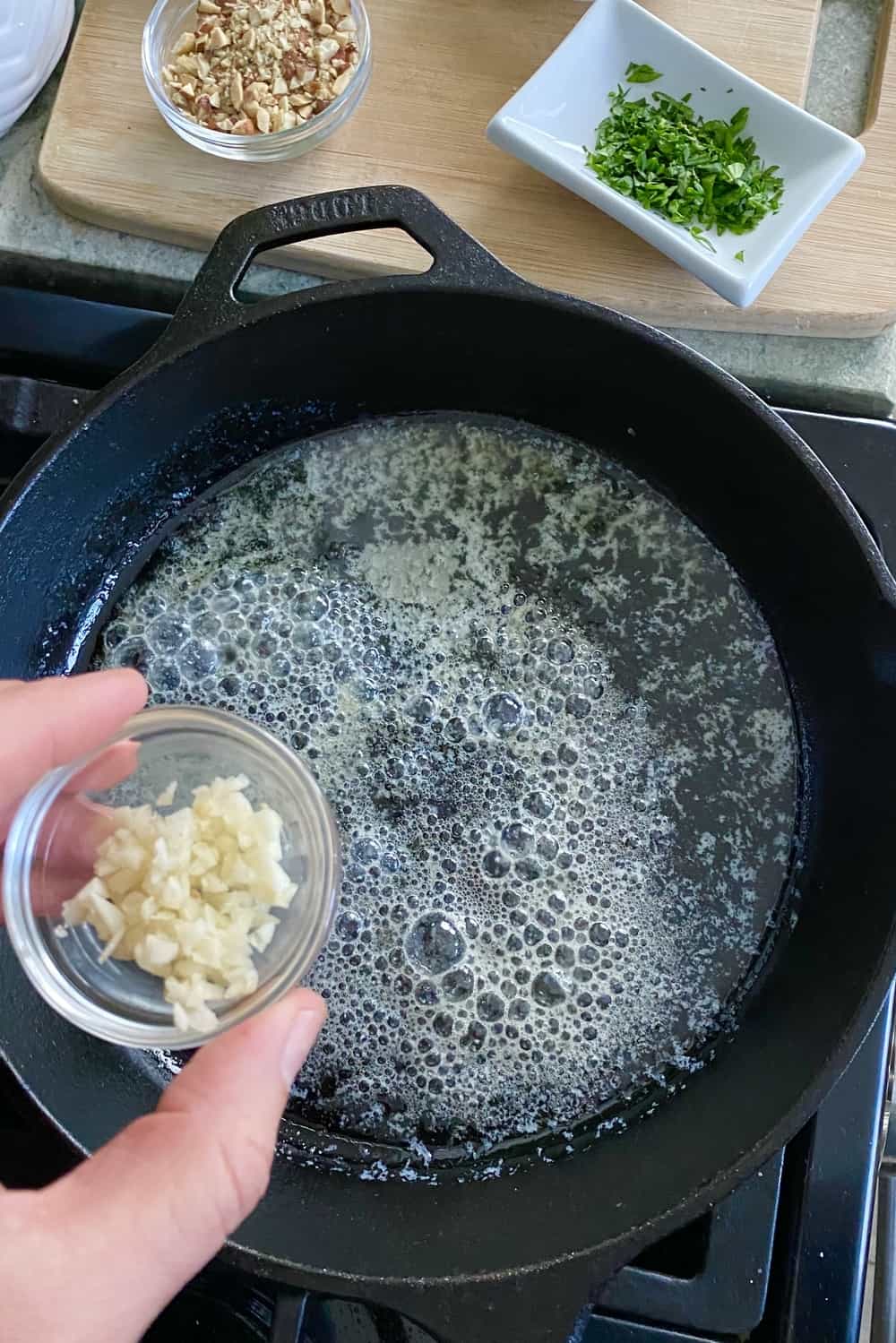 Adding chopped garlic to a cast iron skillet with melted butter.