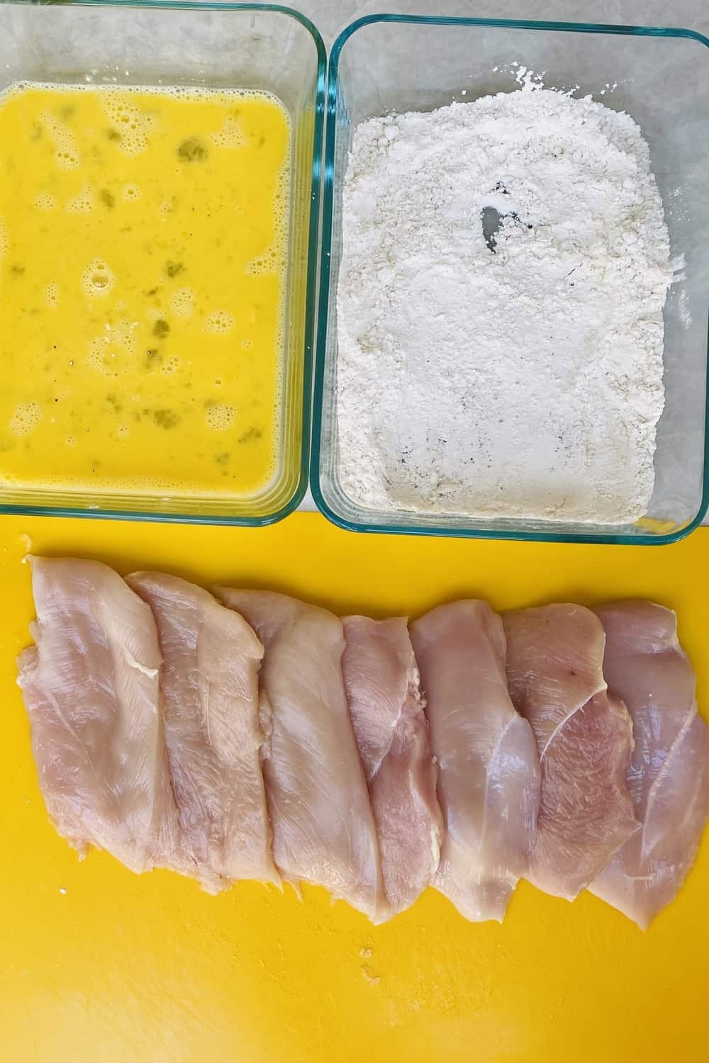 Chicken cutlets with beaten eggs, and flour on a counter.