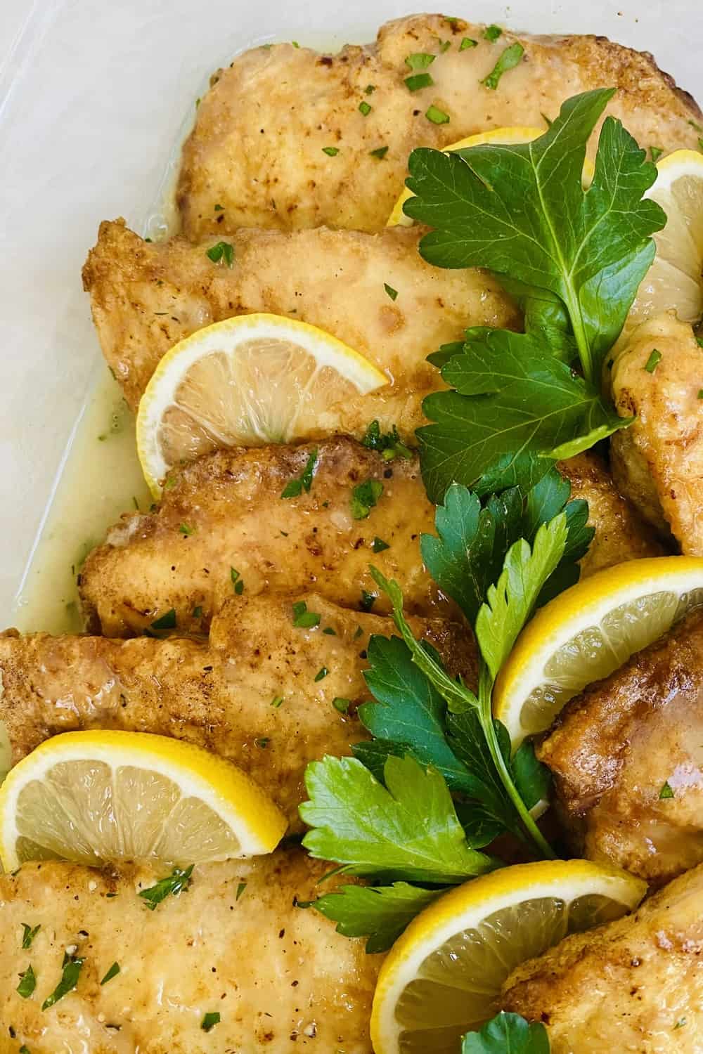 Egg battered chicken that's on a plate with lemon slices.