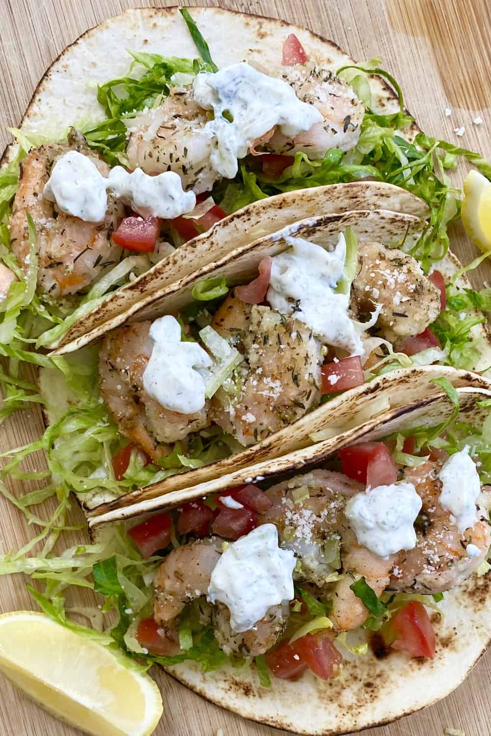 3 Mediterranean shrimp tacos with tzatziki sauce on a cutting board.