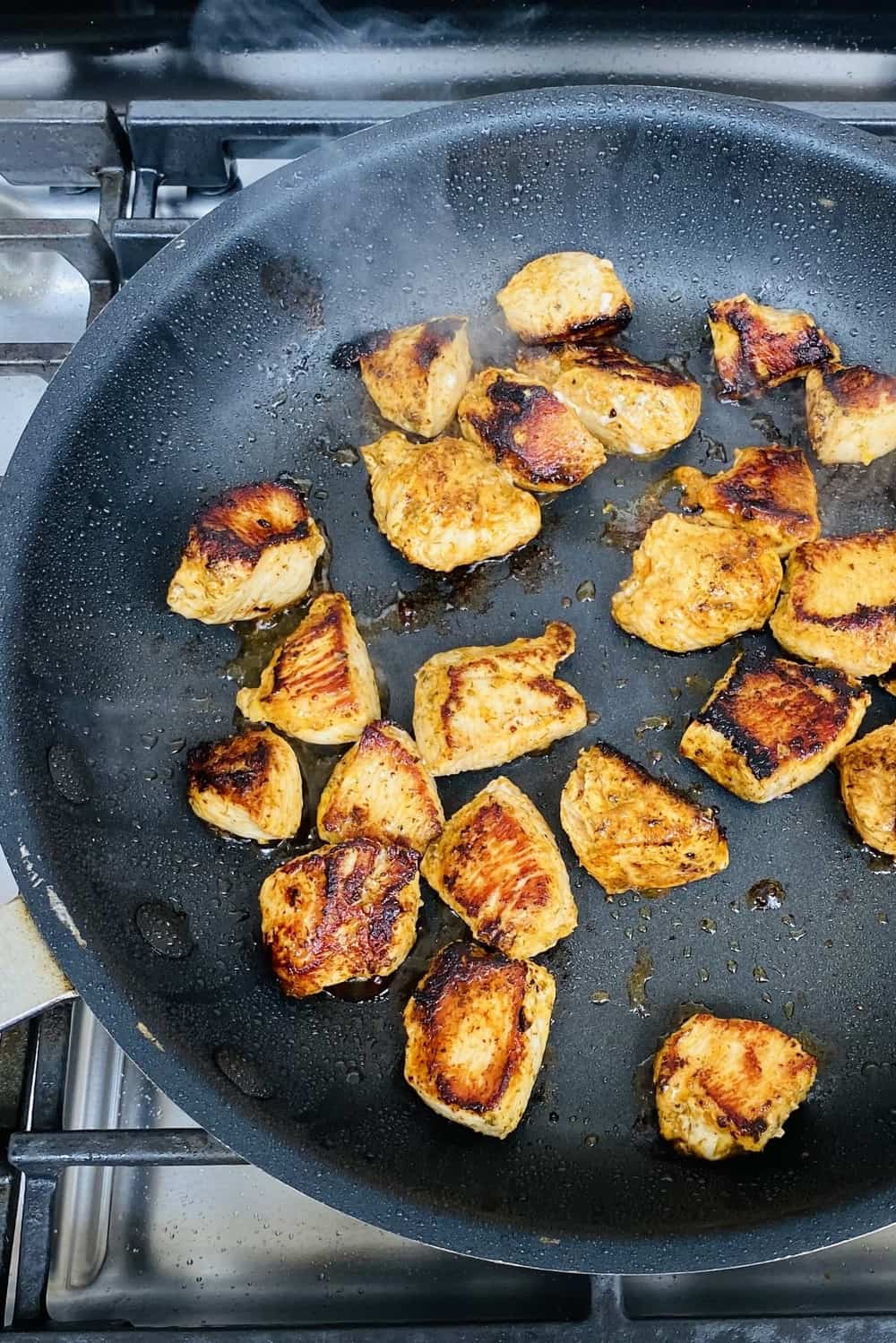 Seared and charred lemon herb chicken in a nonstick pan.