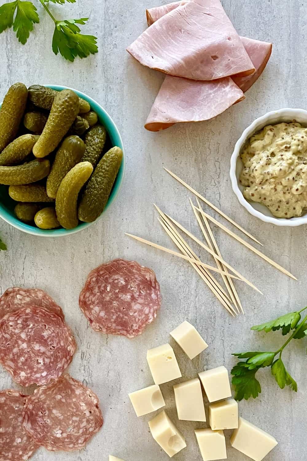 Ham slices, Swiss cheese, salami, dill pickles, mustard on a marble counter.