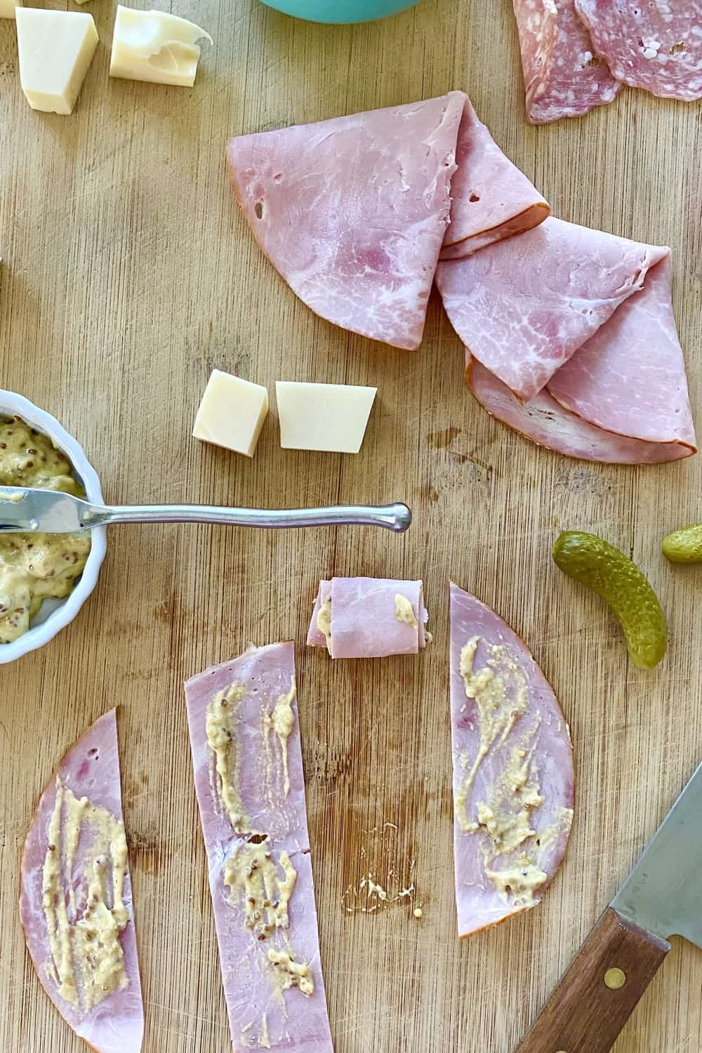 Strips of ham spread with mustard with small pickles and cheese cubes.