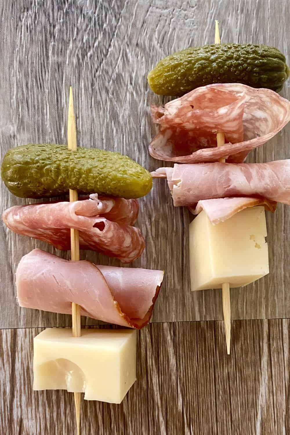 A toothpick with a cheese cube, ham roll up, salami roll up and a small pickle.