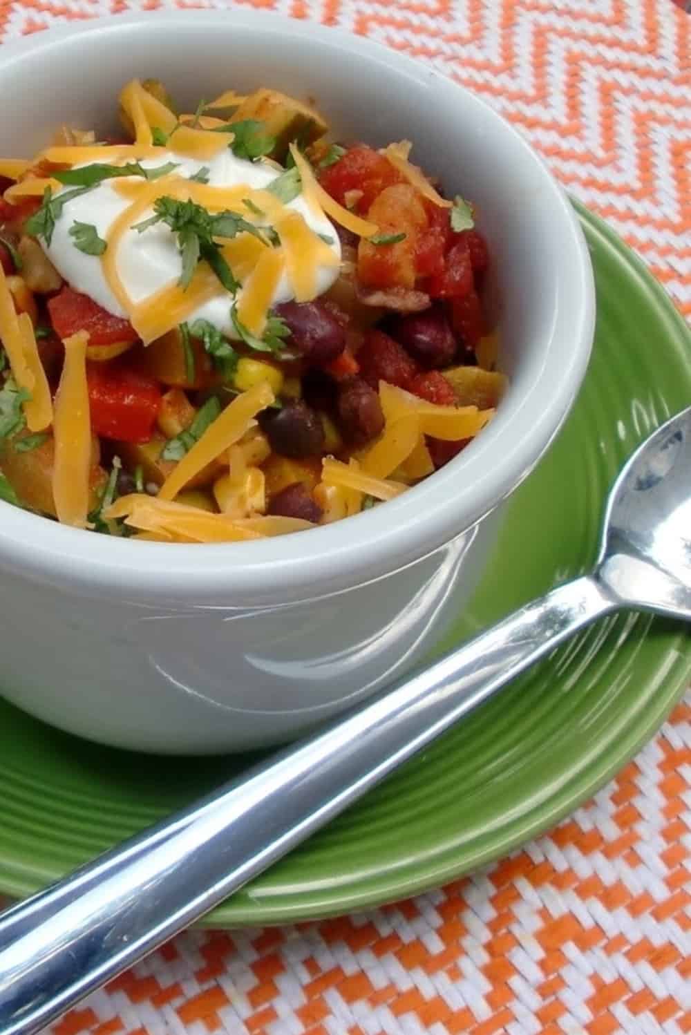 A bowl of vegetable chili with shredded cheese and sour cream.