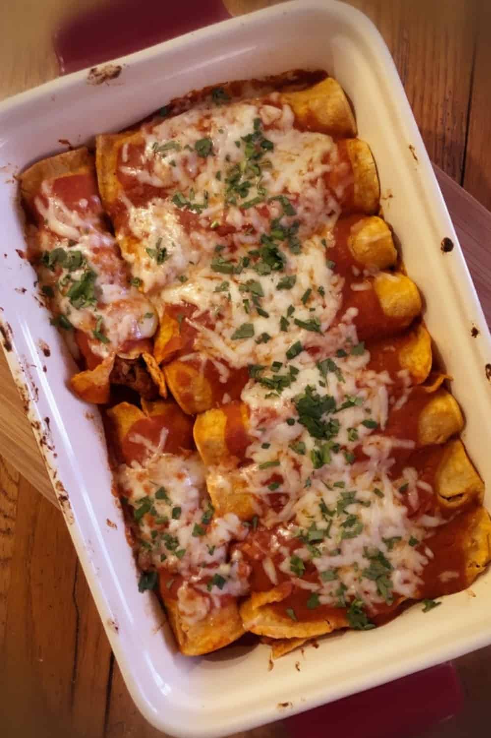 A white baking dish with ground beef enchiladas.