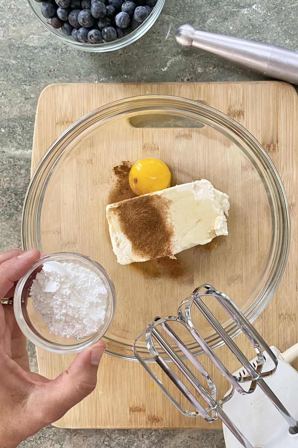 Adding powdered sugar to egg and cream cheese in a bowl.