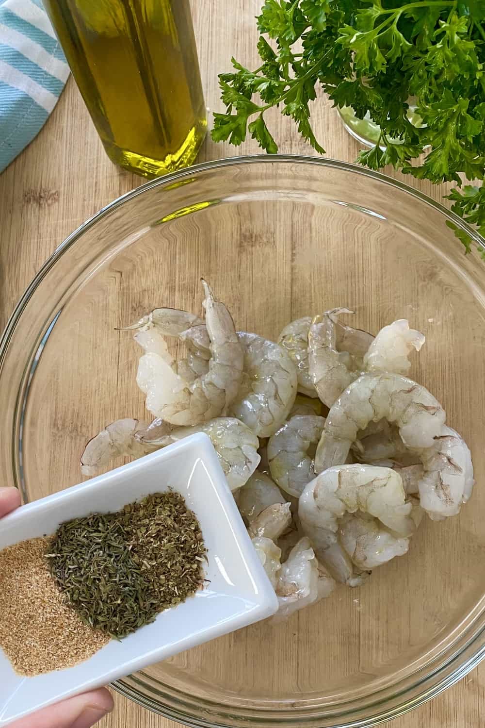 Adding spices to raw shrimp in a bowl.