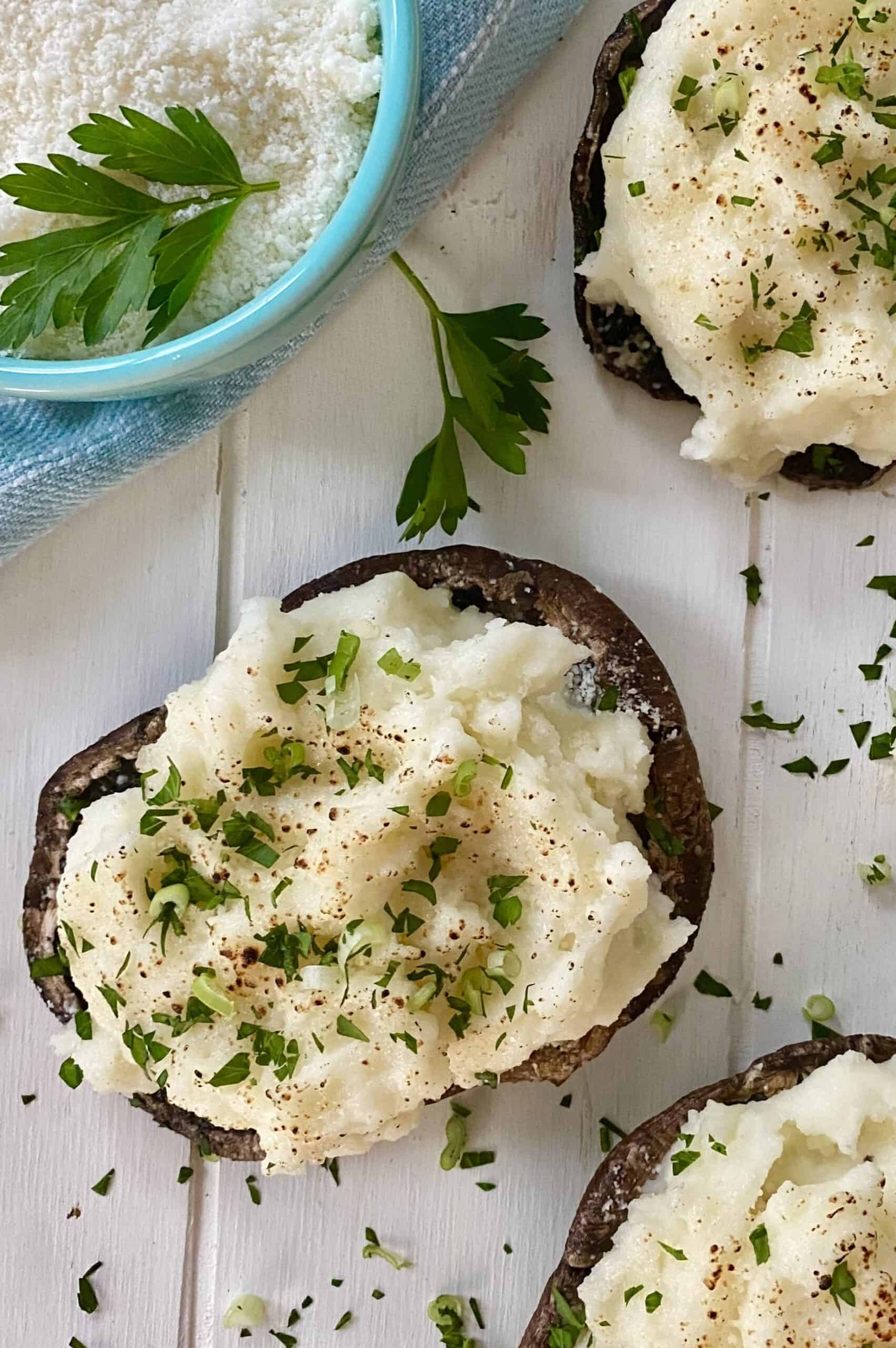 A bowl of grated parmesan cheese and 2 stuffed caps of mushrooms.