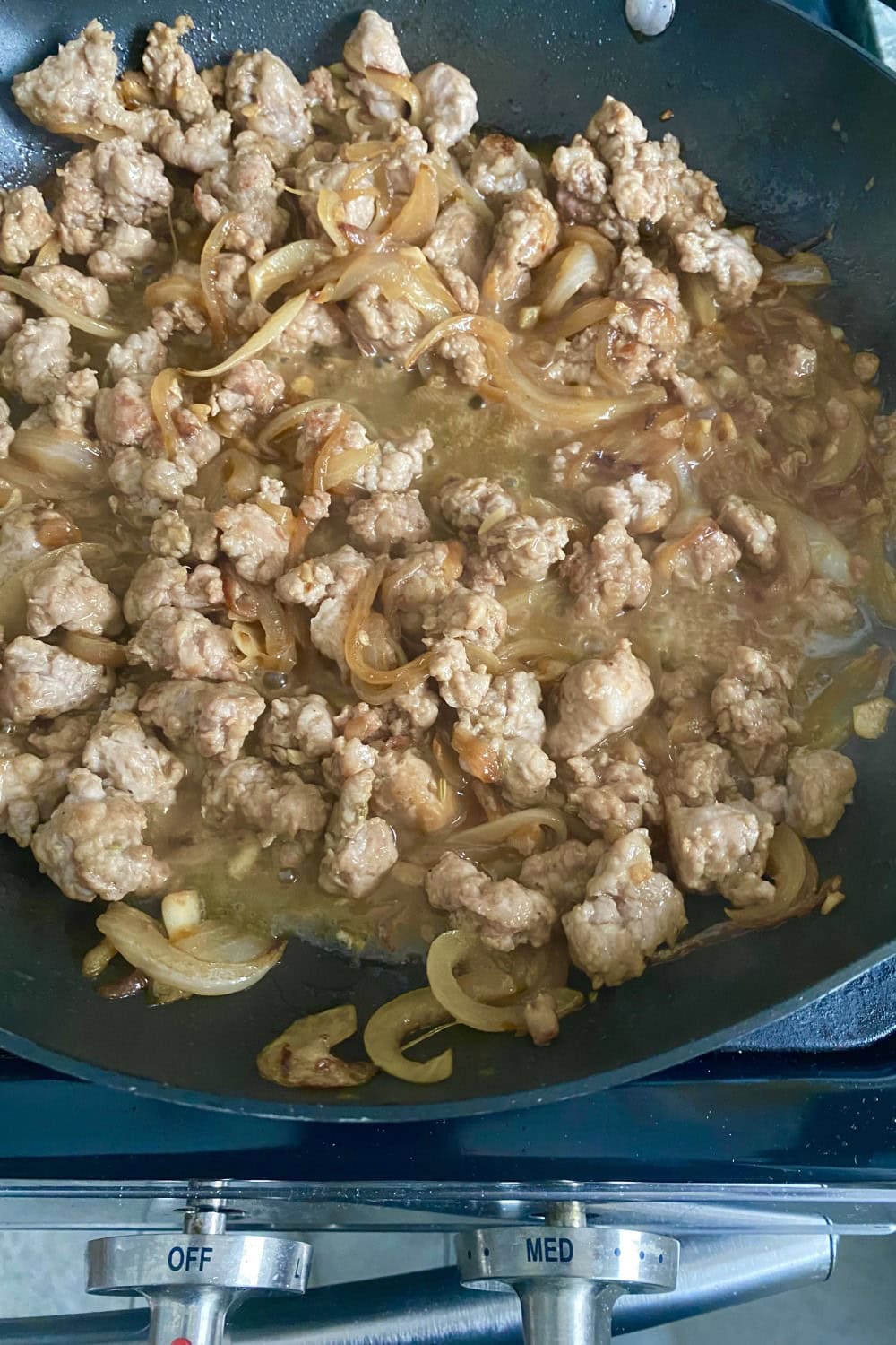 Cooked and crumbled sausage with onions and stock in a pan.