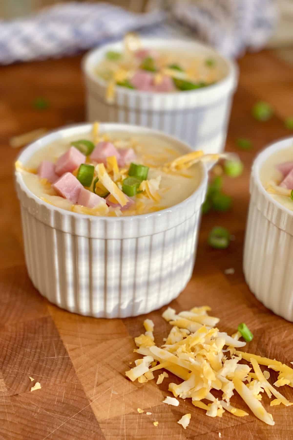 3 bowls of creamy soup topped with ham and shredded cheese.