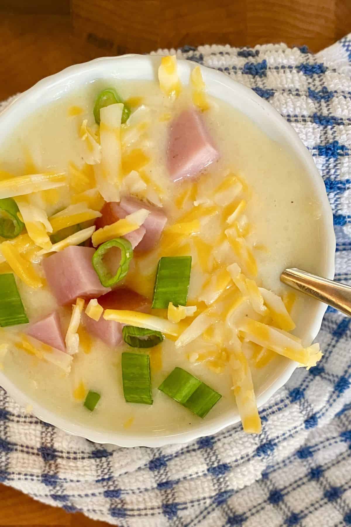 bowl of cheesy ham and potato soup topped with cheese, ham and scallions.