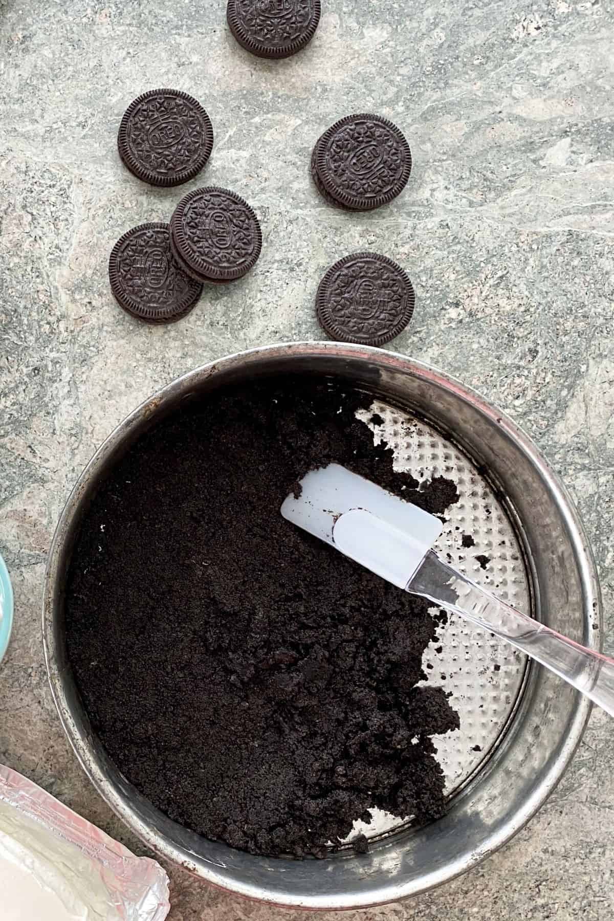 spreading Oreo cookie crust in a springform pan.