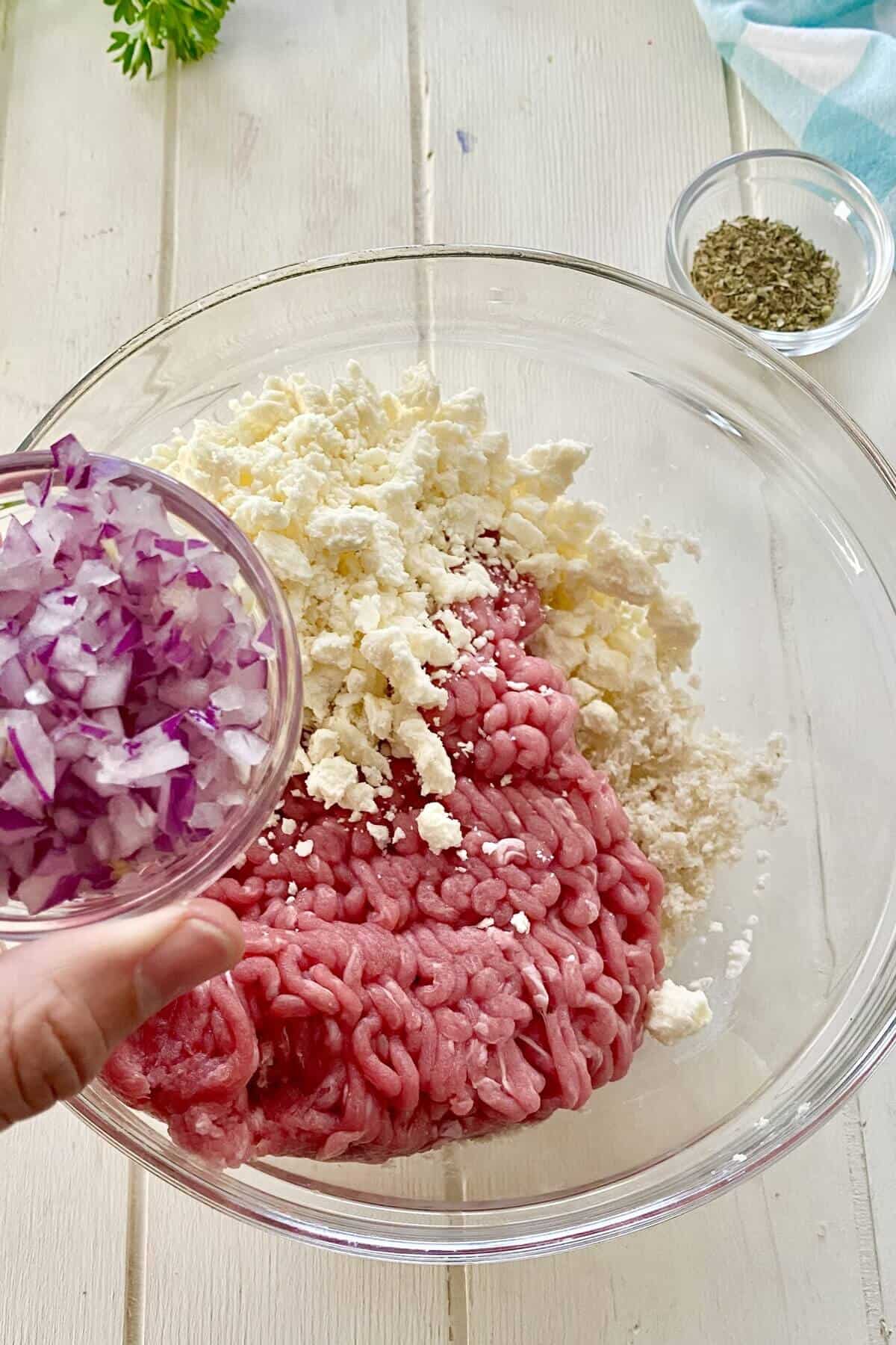 adding chopped onions to ground turkey and feta.