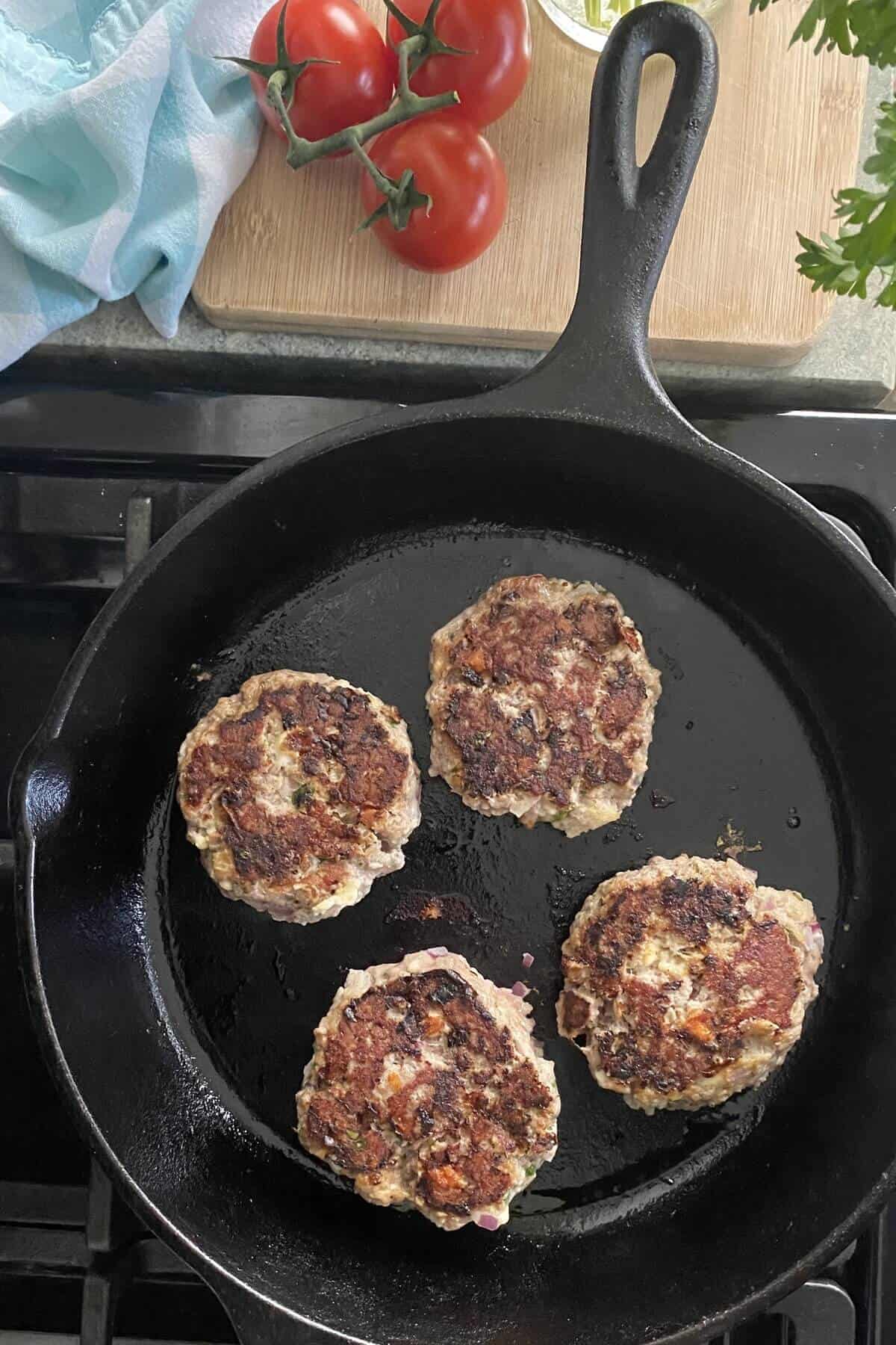 cooking Greek turkey burgers in a cast iron skillet.