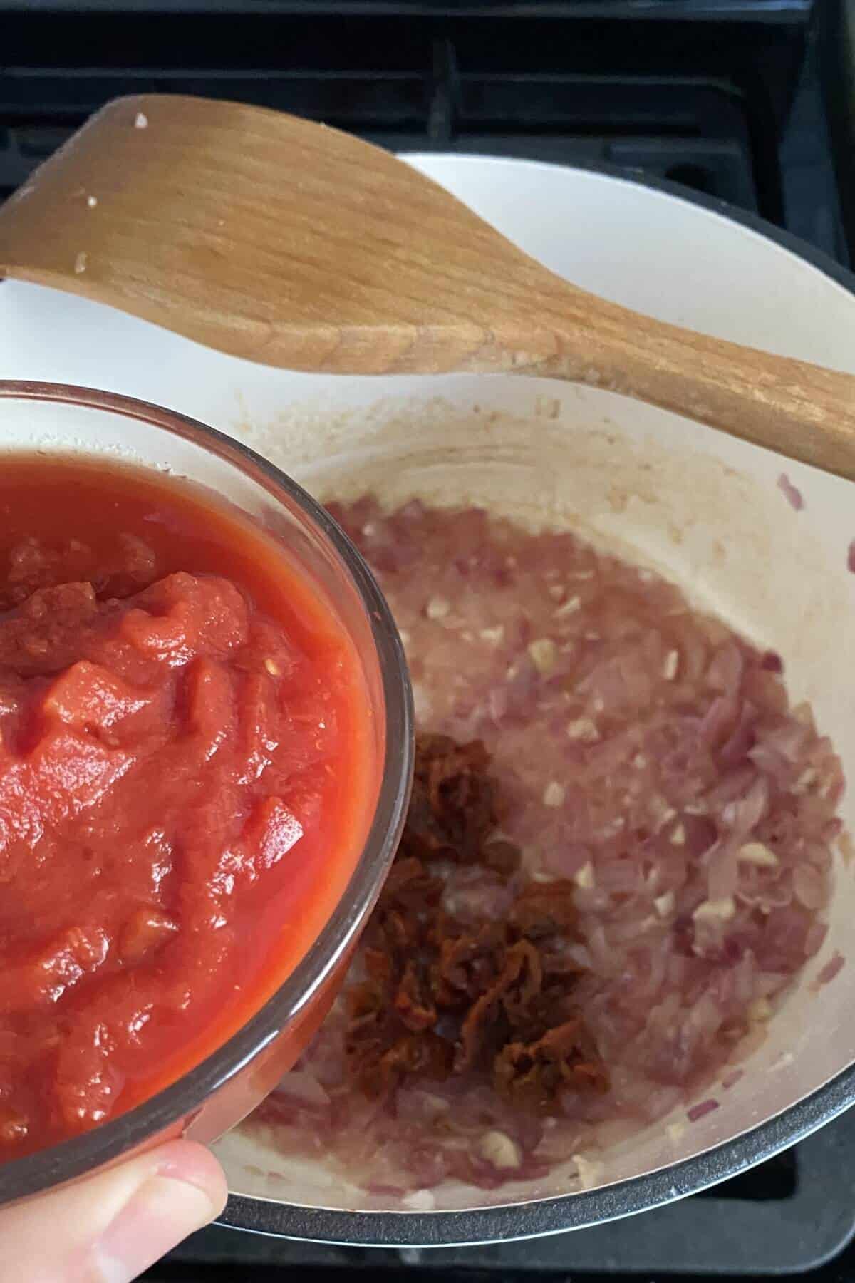 A bowl of crushed tomatoes and pan of sauteed onions and garlic.
