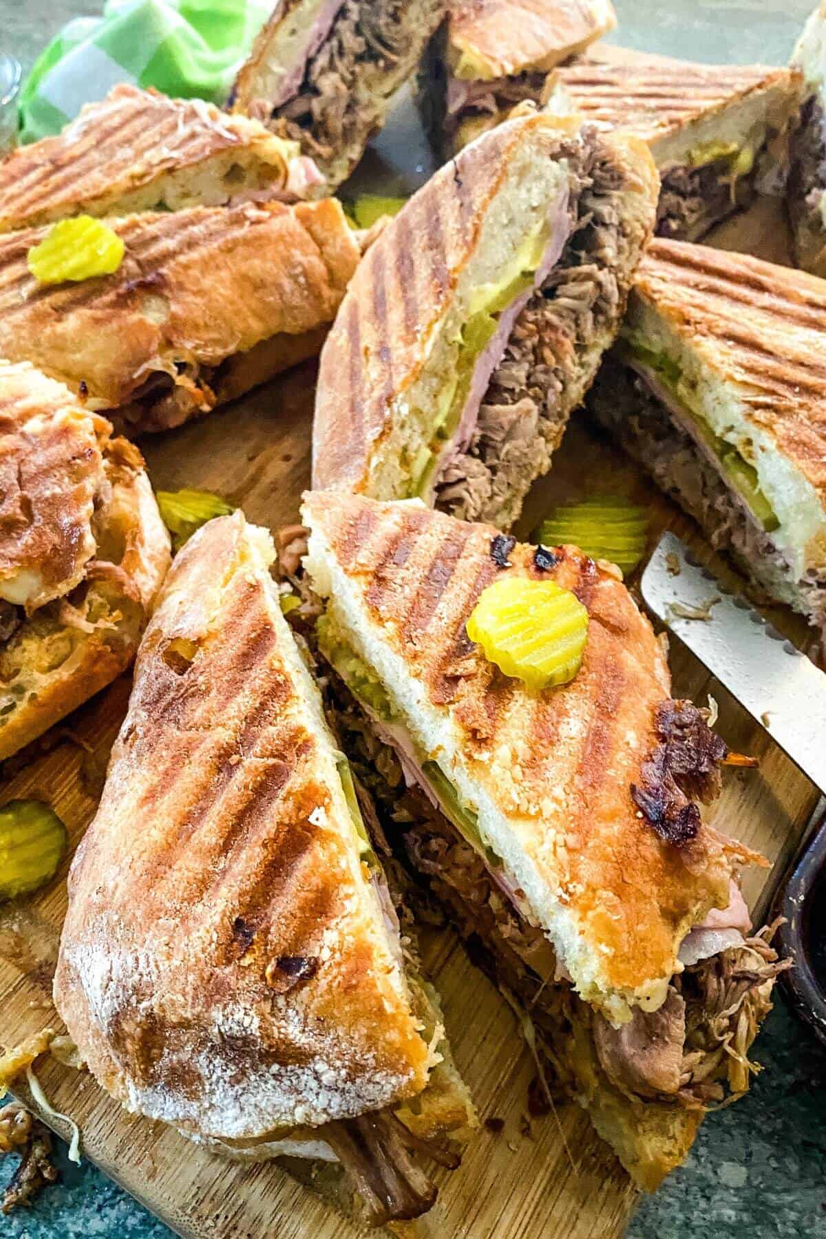 Cuban pork sandwiches with pickles on a cutting board.