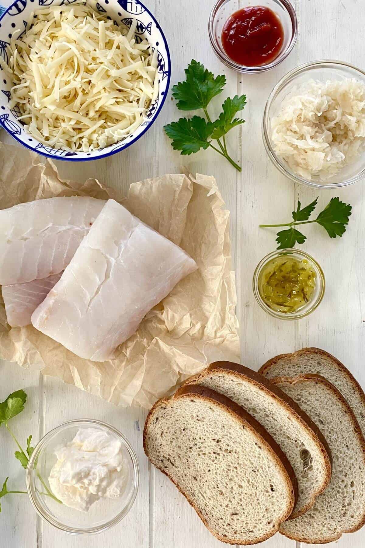 Wild cod, rye bread, mayonnaise, Swiss cheese, sauerkraut on a wood counter.
