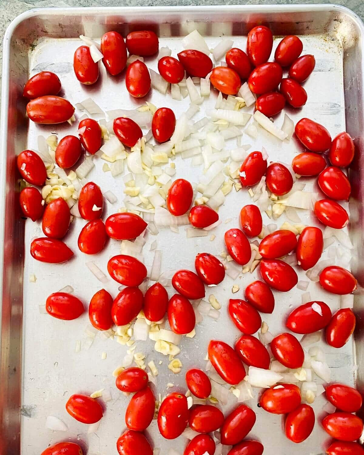 cherry tomatoes, onion and garlic on a baking sheet.