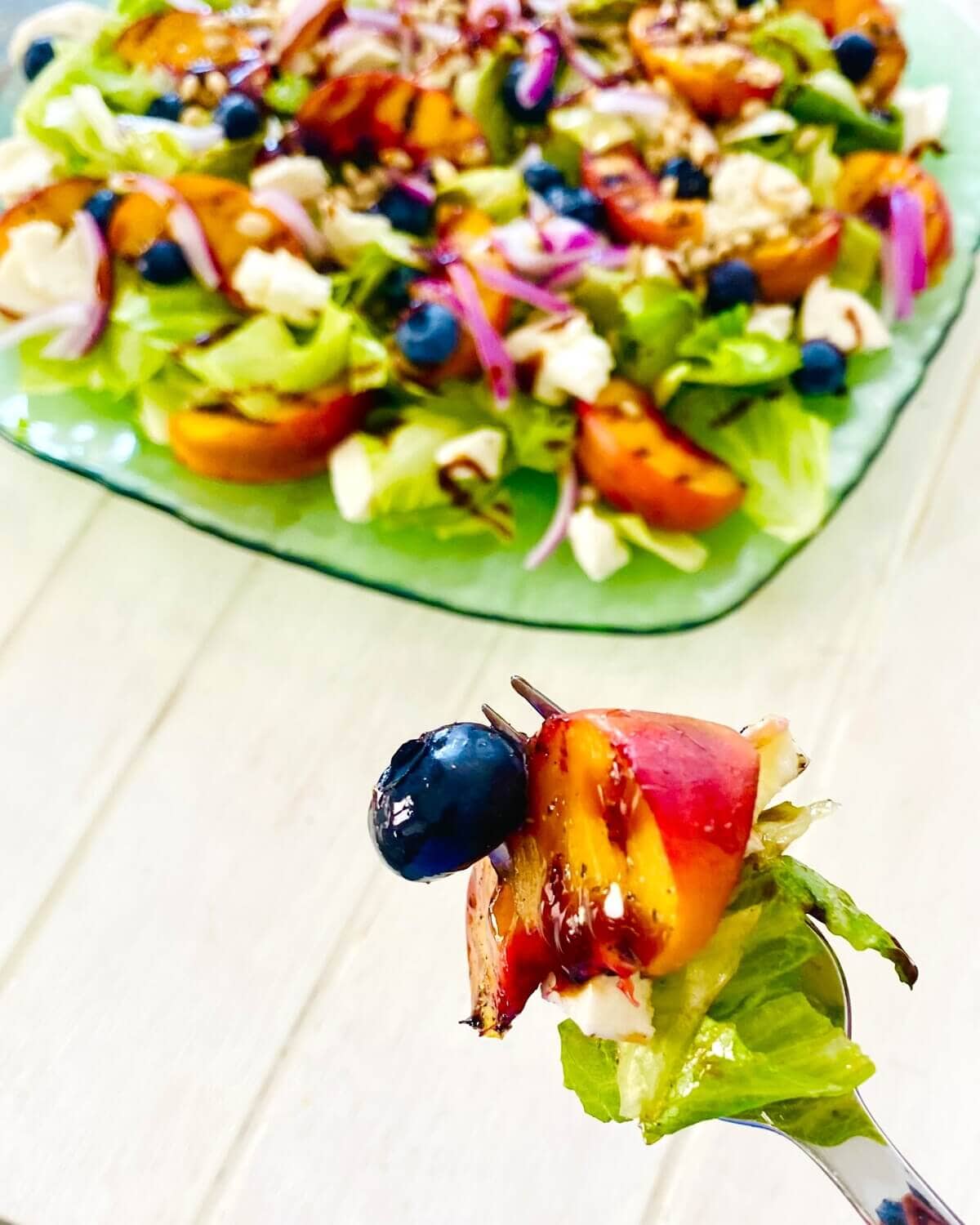 a fork with a blueberry, lettuce, grilled peach and red onion.