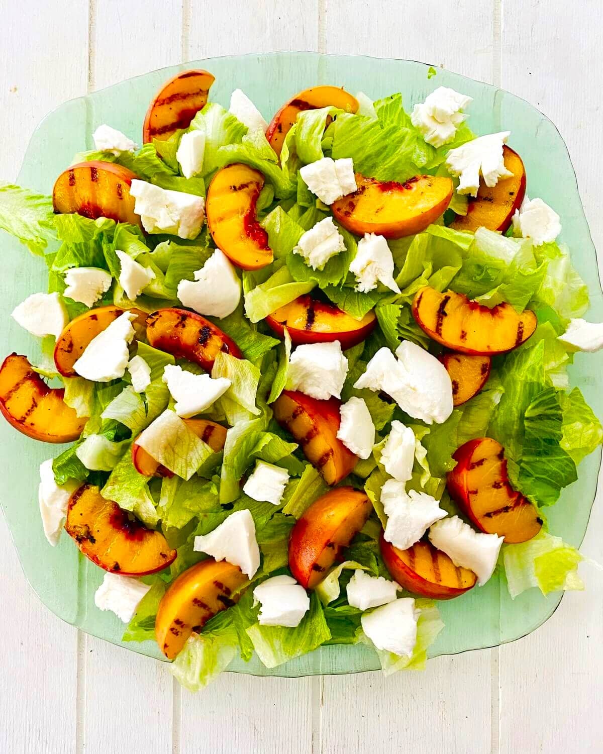 A platter with lettuce, grilled peaches and fresh mozzarella.