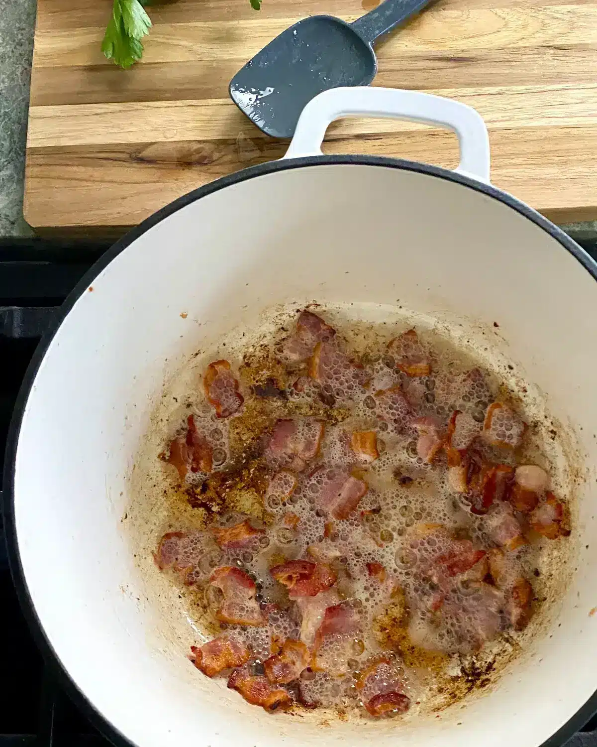 Cooking bacon in a white Dutch oven.