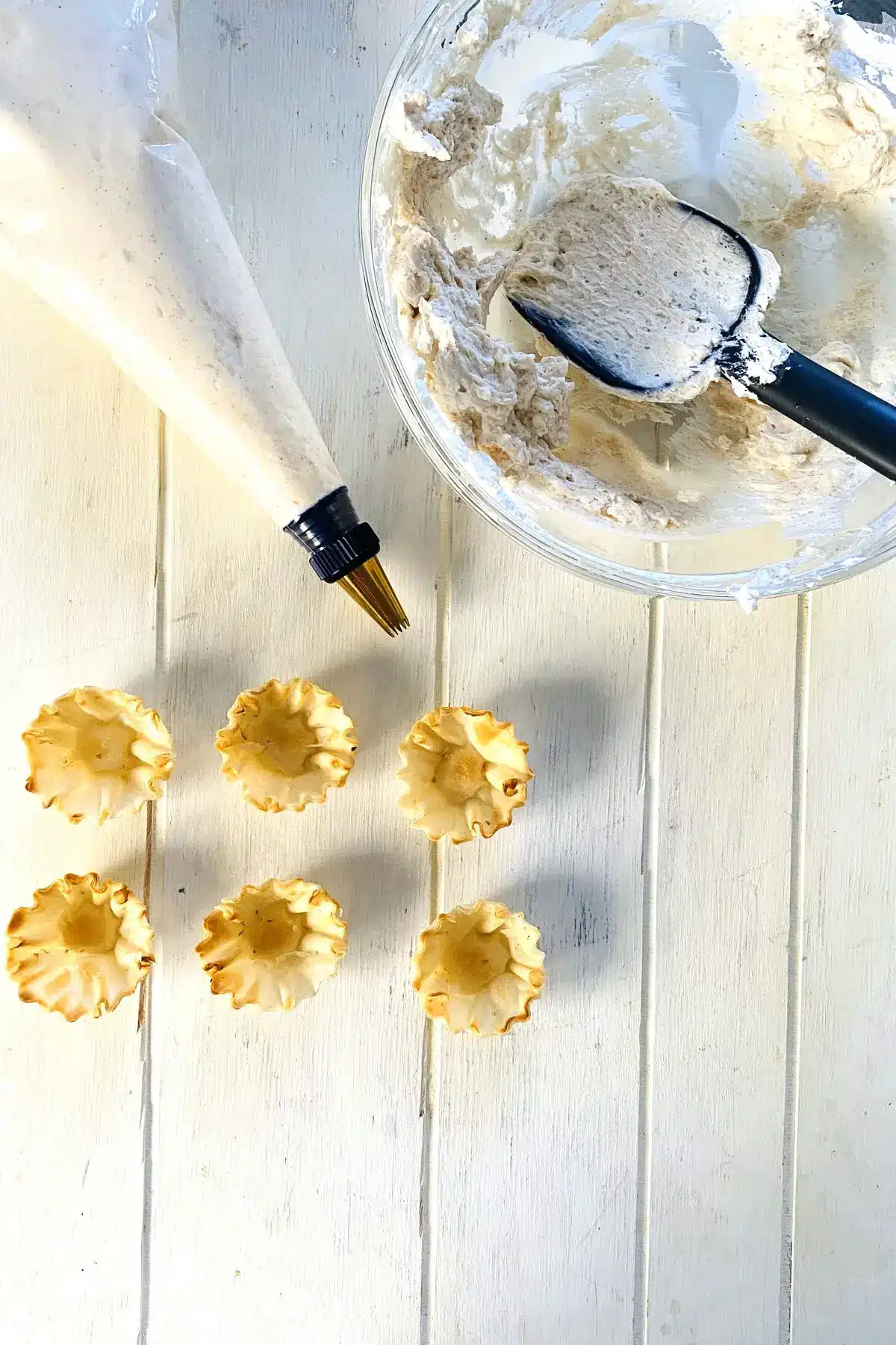 Piping bag filled with cheesecake filling and empty phyllo cups.