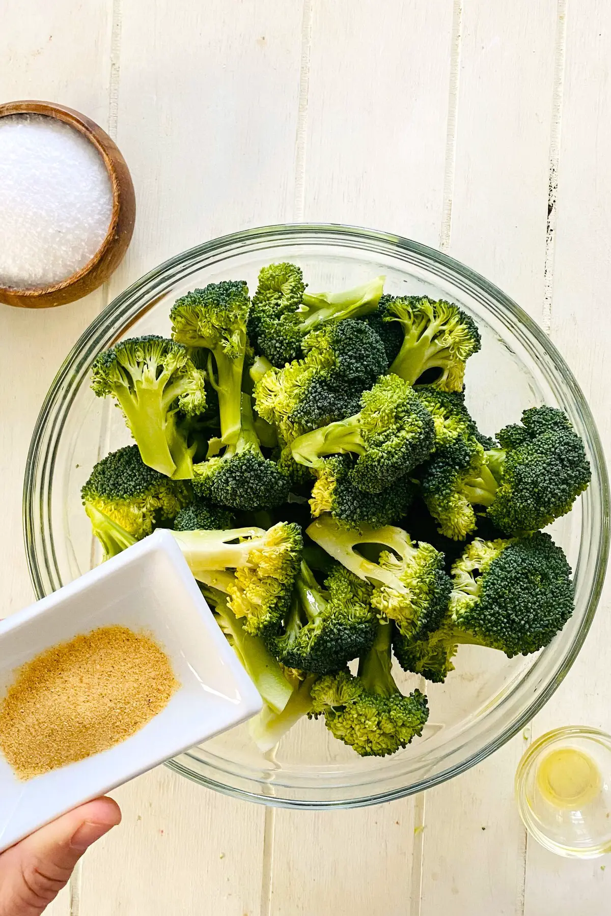 adding garlic powder to raw broccoli.