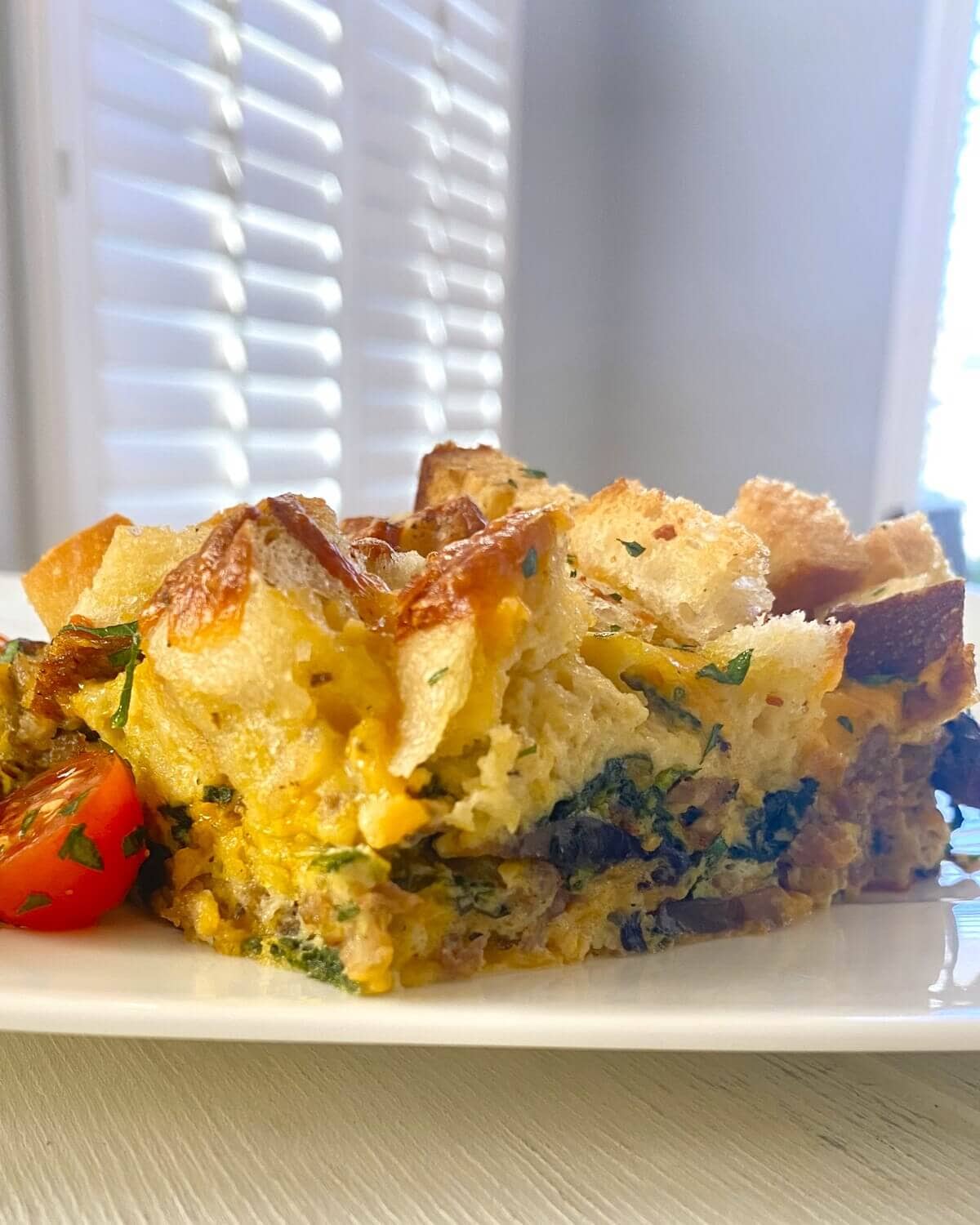 slice of egg casserole with croutons and cherry tomatoes on side.