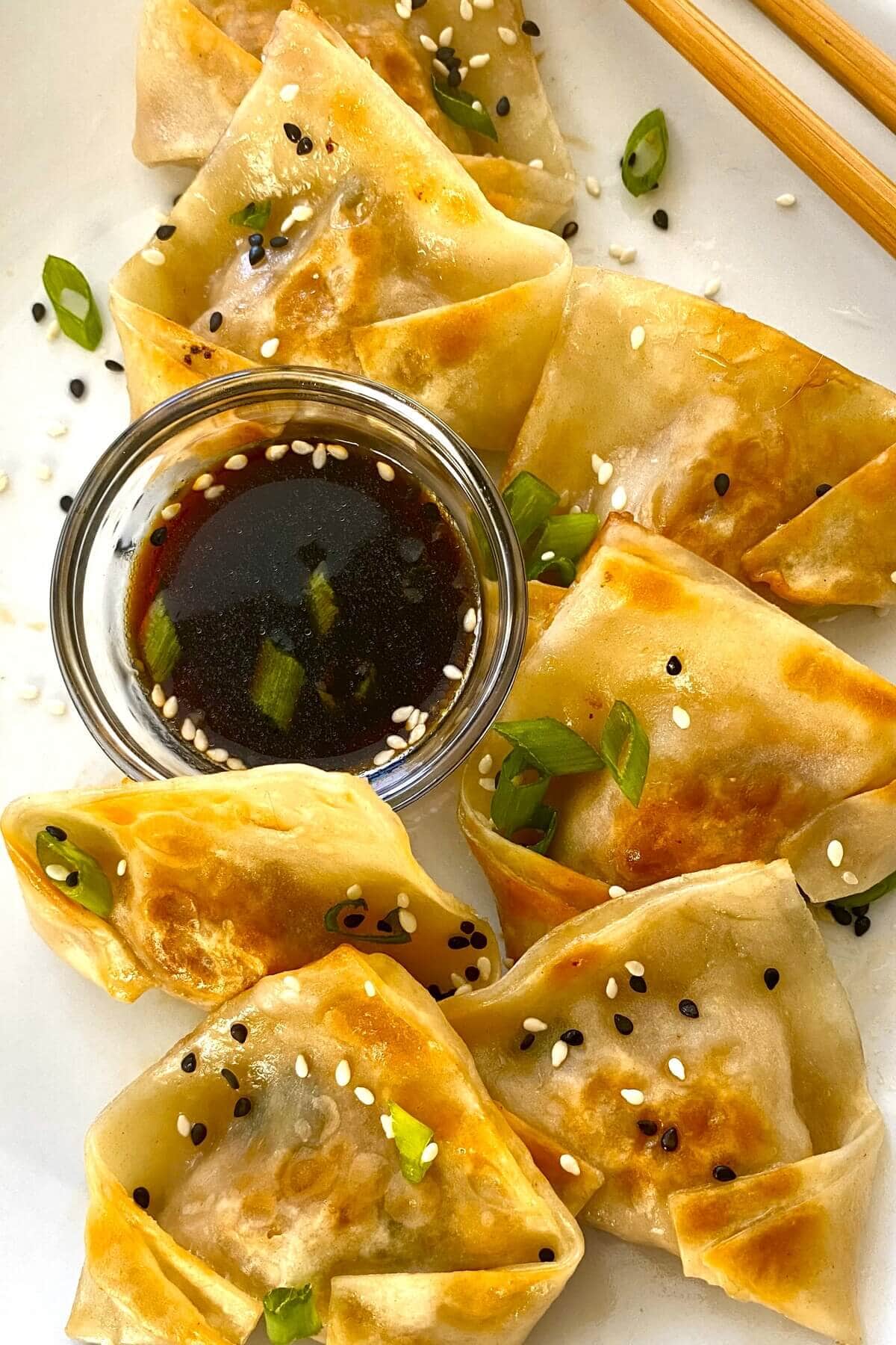 Pork potstickers on a plate with dipping sauce and chopsticks.