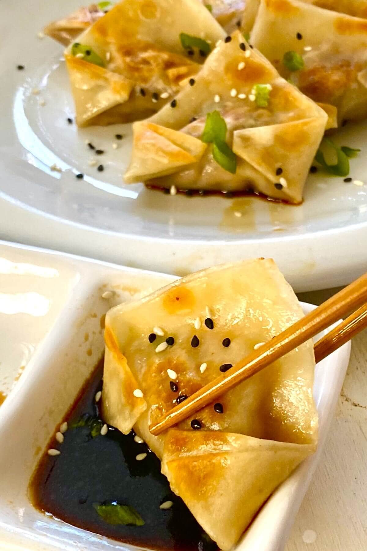 One potsticker with chopsticks and dipping sauce.