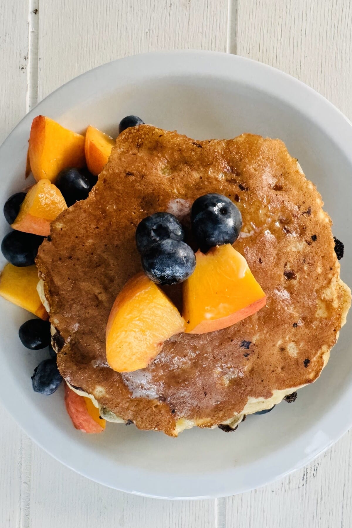 A pancake with cut up peaches and blueberries.