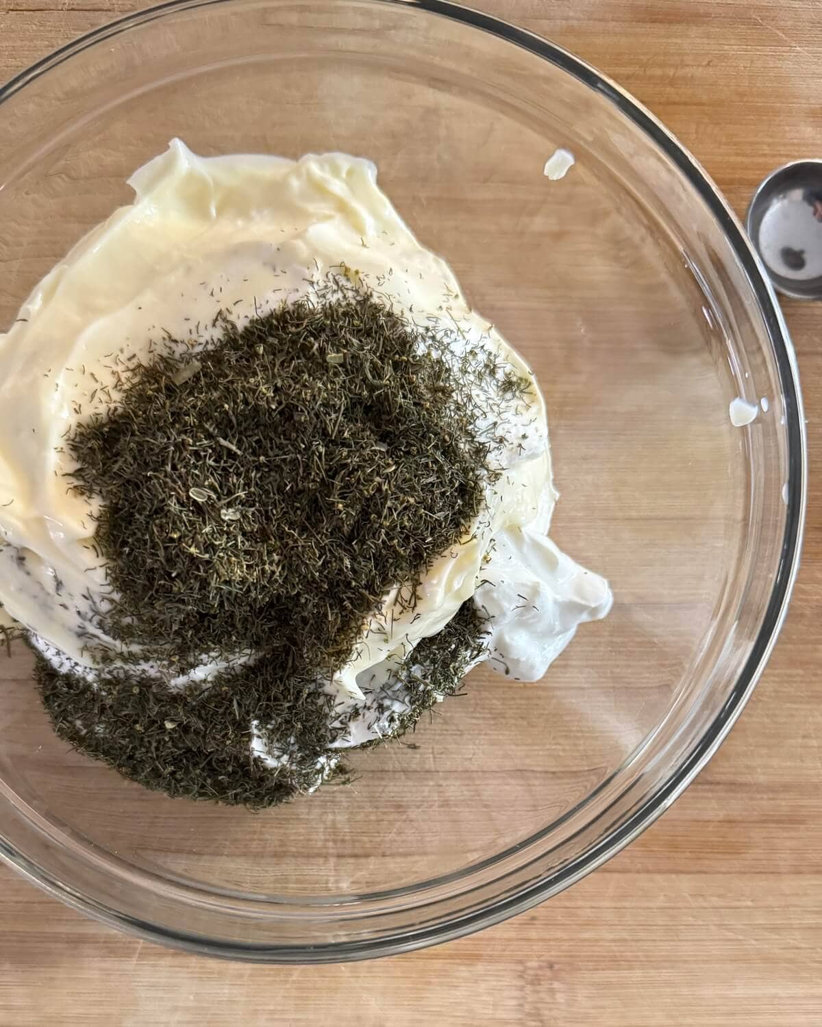 Mayonnaise, sour cream and dried dill in a glass bowl.