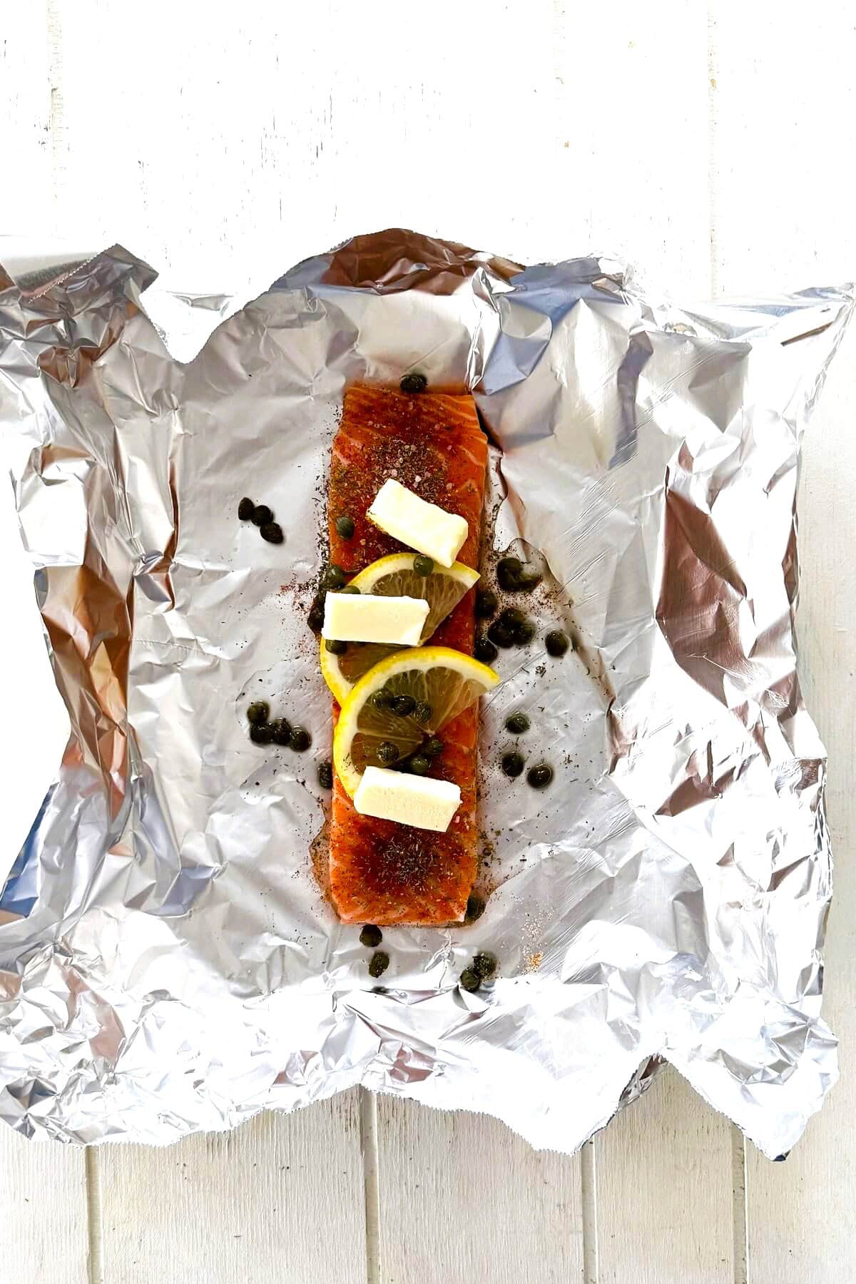 An unbaked salmon fillet in foil with butter and lemons.