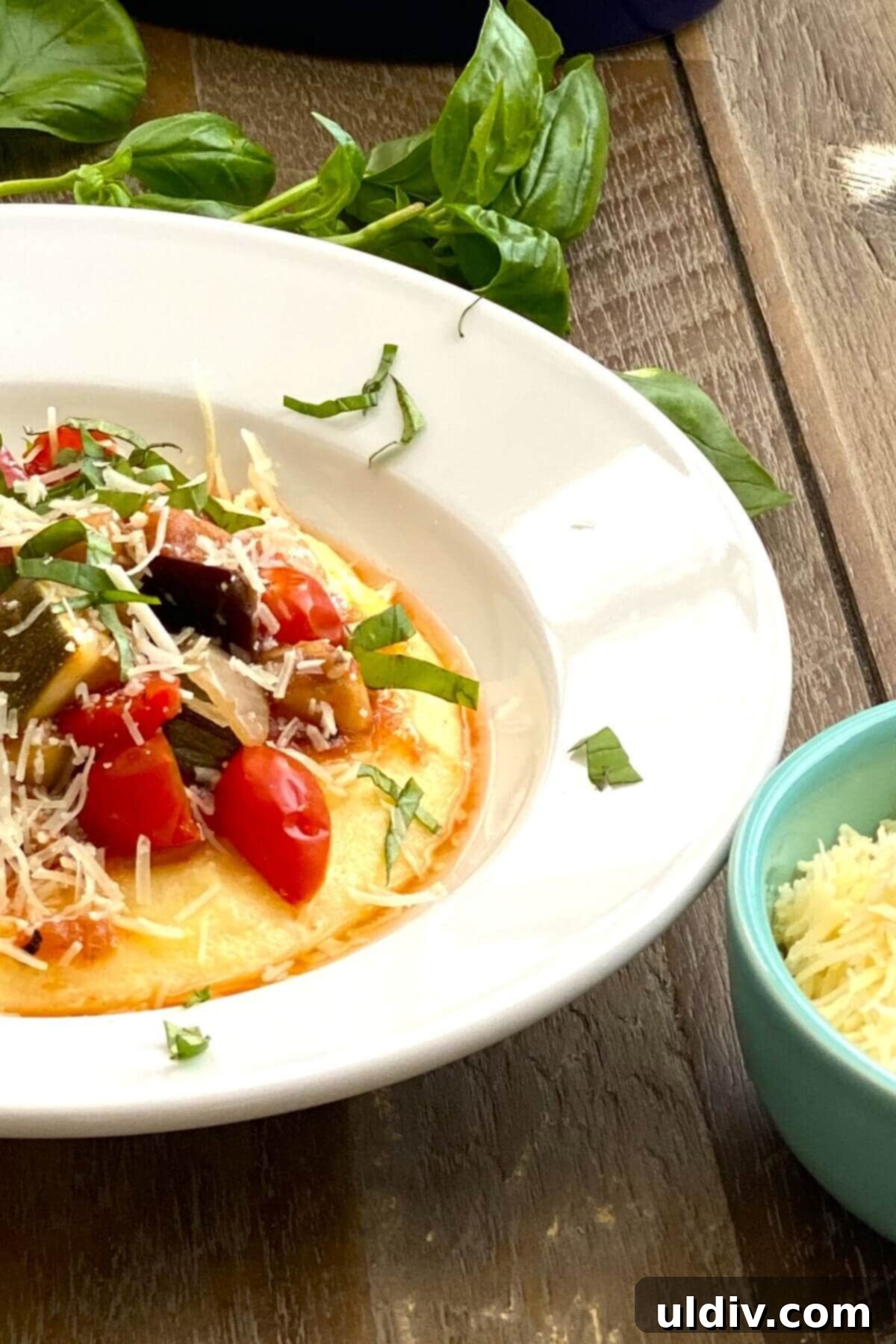A dish of ratatouille with polenta, fresh basil and parmesan cheese.
