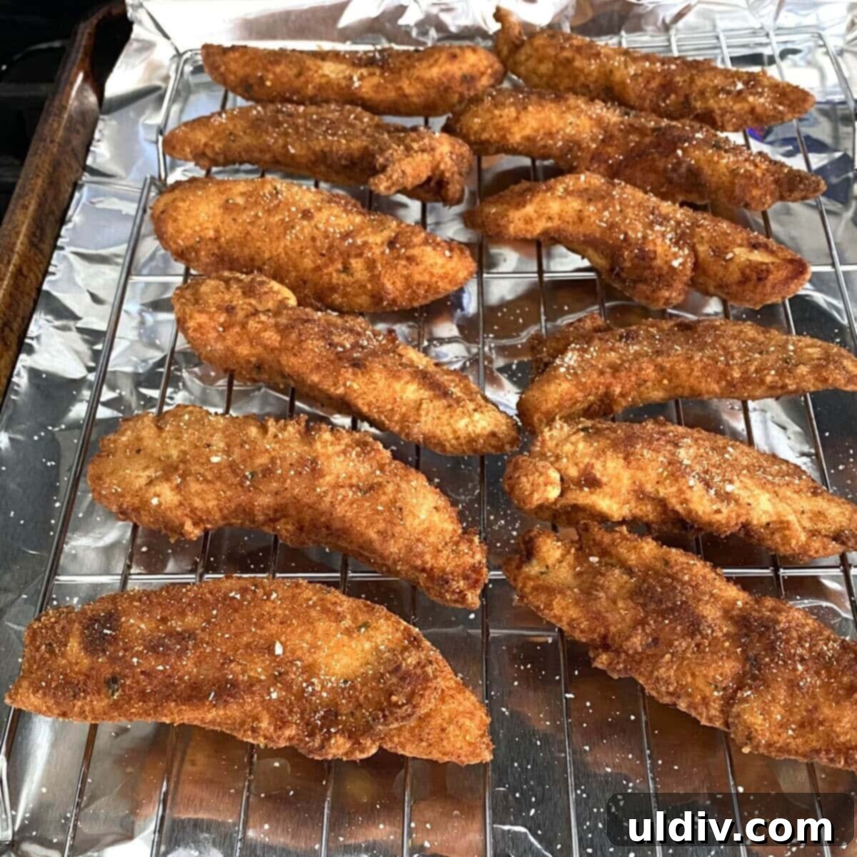 Golden Crispy Buttermilk Chicken Tenders 4 Crispy buttermilk fried chicken tenders neatly arranged on a cooling rack over a baking sheet, allowing excess oil to drain.